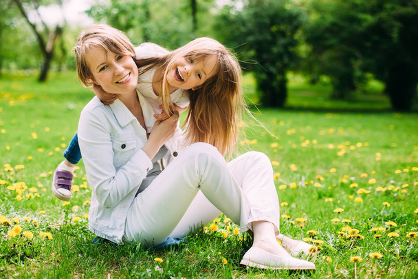 обнимает счастливых мать и дочь для прогулки в парке по зеленой лужайке
 - Фото, изображение