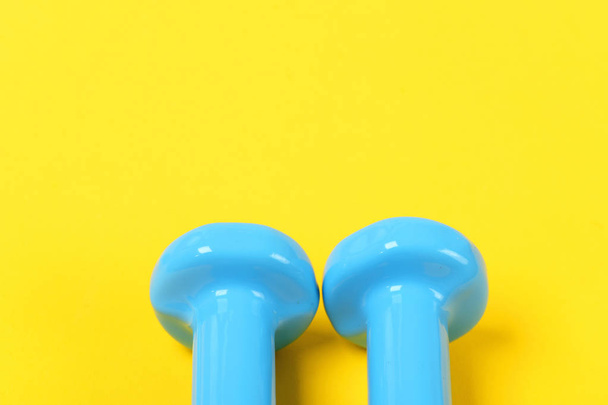 Tops of blue fixed weight dumbbells on yellow background - Φωτογραφία, εικόνα