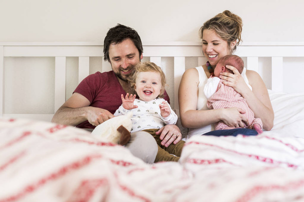 Young parents in bed with their cute little children - Foto, afbeelding