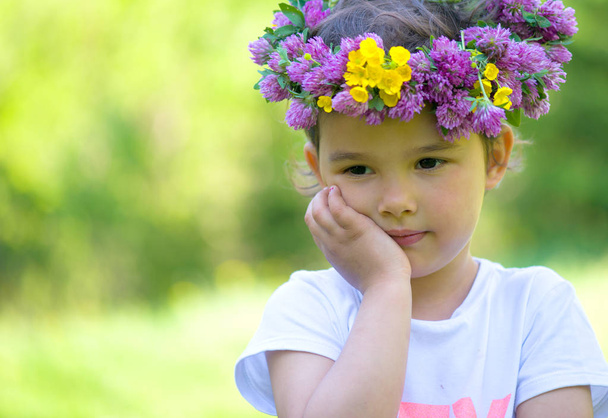 Portret van een vrolijk meisje met een krans van bloemen op haar hoofd - Foto, afbeelding