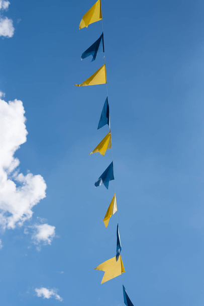 mavi ve sarı kiraz kuşu mavi yaz gökyüzüne karşı lunapark Festivali'nde rüzgarda sallayarak ipte bayraklar  - Fotoğraf, Görsel
