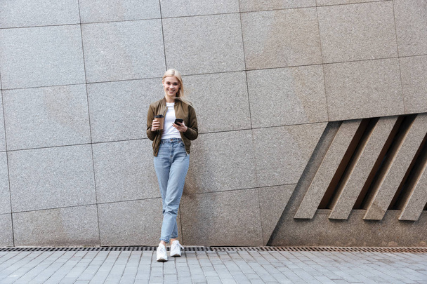 Full-length shot of young woman with cup of coffee and smartphone - Photo, image