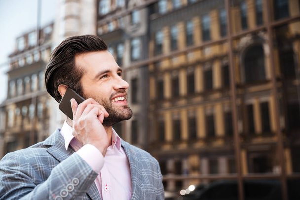 Ελκυστική γενειοφόρος άνδρας στο σακάκι μιλάτε στο κινητό τηλέφωνο - Φωτογραφία, εικόνα