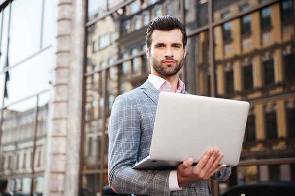 Portrait of a young handsome man in jacket holding laptop - Foto, Imagem