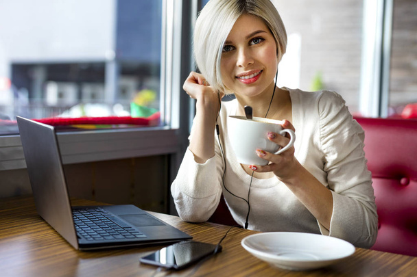Красива молода жінка з кавові чашки і ноутбук в кафе - Фото, зображення