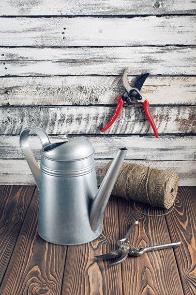 Watering-can and garden pruner on the worn wooden surface. - Photo, Image