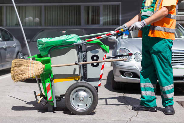 Εργαζόμενος από την εταιρεία καθαρισμού σε πράσινη στολή με κάδο απορριμμάτων. - Φωτογραφία, εικόνα