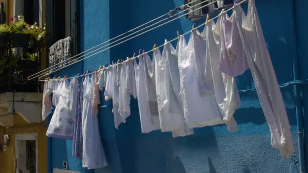 Καθαρά ρούχα φτερουγίσματα ανέμου, κρέμεται από φωτεινό μπλε χρωματισμένο σπίτι πρόσοψη - Πλάνα, βίντεο
