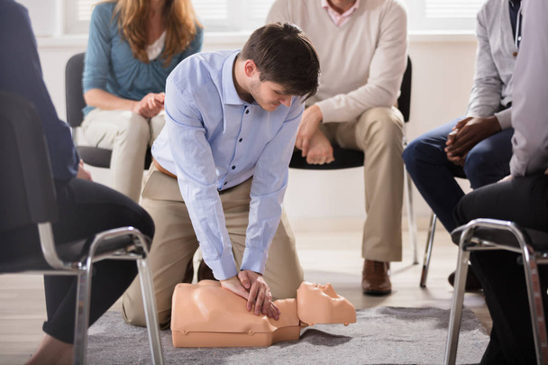 Молодий чоловік інструктор показує тренінги CPR на Даммі своєму студенту
 - Фото, зображення
