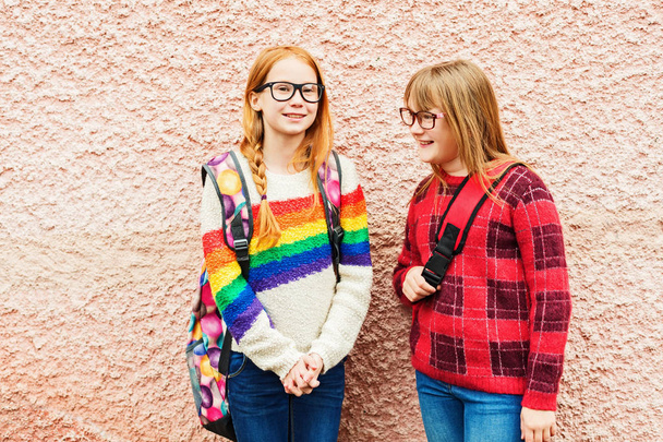 Groep van twee schattige jongen meisjes buitenshuis poseren tegen roze muur, het dragen van bril, school rugzakken en heldere kleurrijke truien, terug naar school concept - Foto, afbeelding