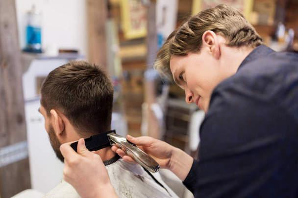 man and barber with trimmer cutting hair at salon - Φωτογραφία, εικόνα