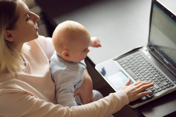 Young mother in home office with computer and her baby. Freelancer or blogger, work and child care. - Foto, Imagen