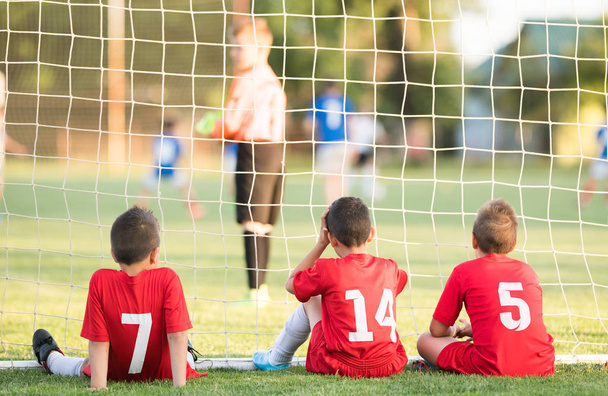 Niños jugadores de fútbol sentados detrás de gol viendo partido de fútbol
  - Foto, imagen
