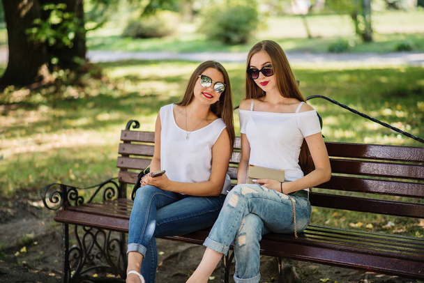 Two fabulous girls sitting on the bench in the park. - Zdjęcie, obraz