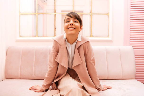 Cute smiling girl in coat sitting on a sofa - Foto, immagini