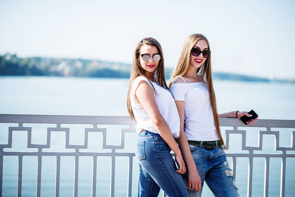 Two beautiful girls wearing sunglasses pose with a lake in the b - Valokuva, kuva