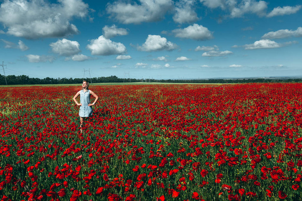 Young woman standing in the field of red poppies against the blue sky scenic landscape concept of outdoor recreation - Photo, Image