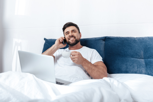 Young man talking on phone in bed - Фото, изображение