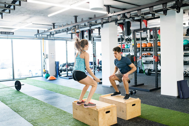 Young fit couple exercising in gym, doing box jumps. - Foto, Imagem