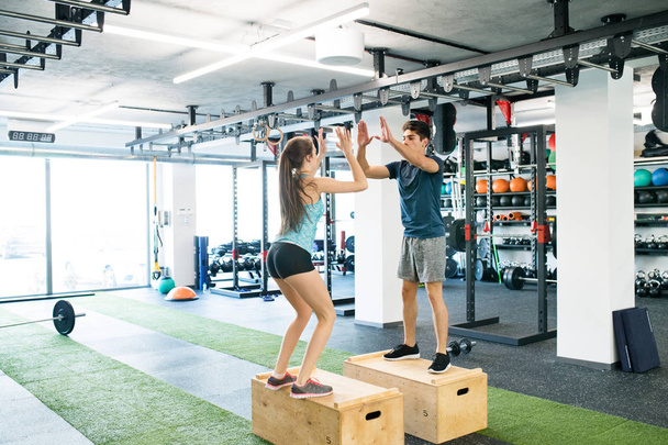 Young fit couple exercising in gym, doing box jumps. - Фото, зображення