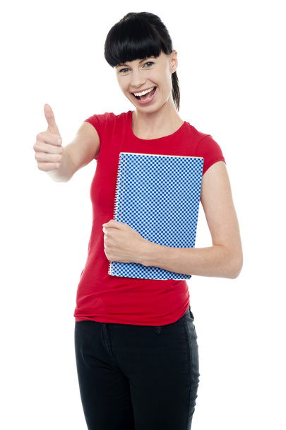 Pretty teenager holding notebook and gesturing thumbs up - Фото, изображение