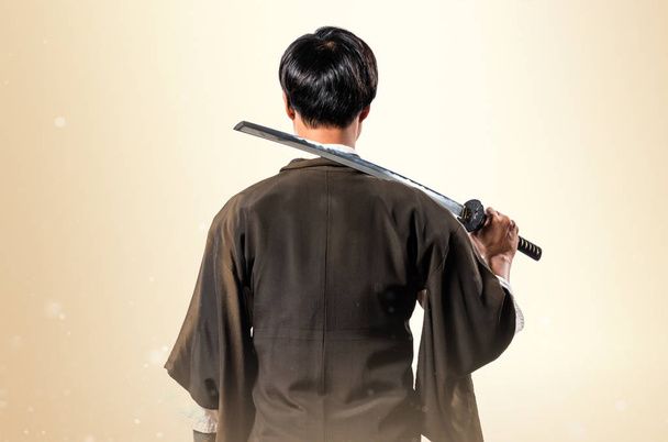 Asian samurai man with katana on ocher background - Foto, afbeelding