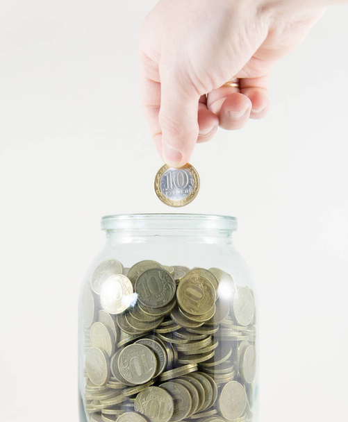 Glass jar with money on a white background. Hand with a coin - 写真・画像