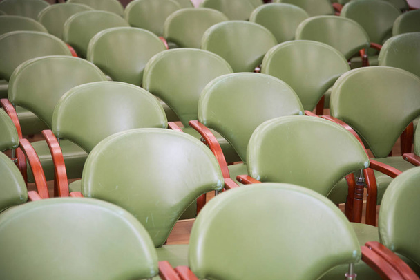 Группа пустых стульев с современной спинкой и зеленой обивкой рядами в неизвестном зале
 - Фото, изображение