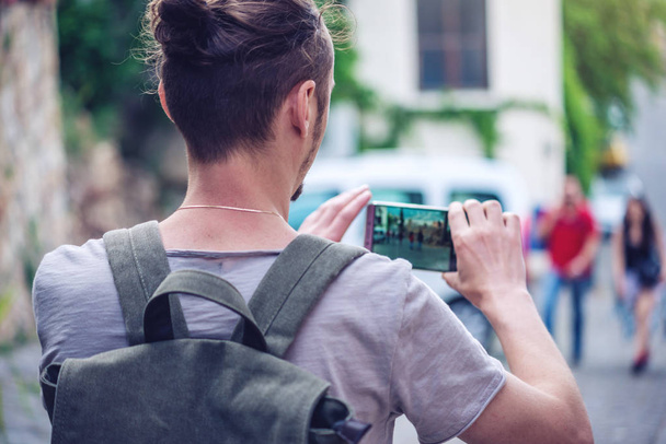 Man backpack makes a photo on your smartphone on a city street - 写真・画像
