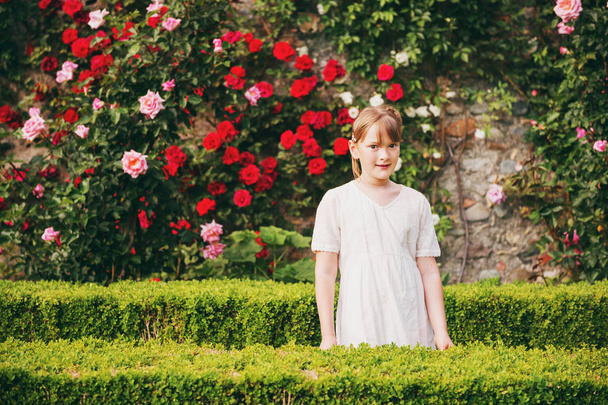 Очаровательная маленькая девочка играет в классическом английском тапиарном саду, одетая в белое винтажное платье
 - Фото, изображение