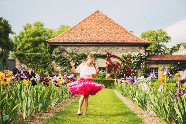 Lief klein jongen meisje dansen in een prachtige bloementuin op een mooie zonnige zomerdag, het dragen van felle roze tutu rok - Foto, afbeelding