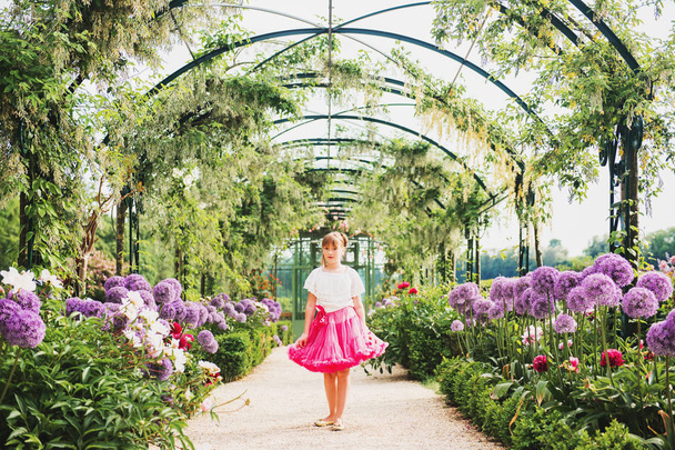 Beyaz gömlek ve parlak pembe tutu etek giyen güzel bir güneşli günde güzel bir çiçek bahçesinde oynayan sevimli küçük kız. Dev allium giganteum çiçekli sokak - Fotoğraf, Görsel