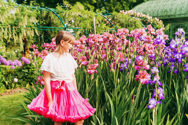 Söpö pieni tyttö leikkii Iris kukka puutarhassa mukava kesäpäivä, yllään valkoinen paita ja kirkas vaaleanpunainen tutu hame
 - Valokuva, kuva