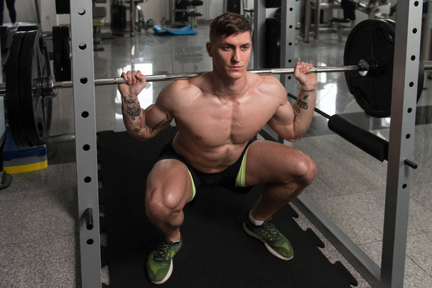 Fitness Man Using Barbell Exercising Legs Inside Gym - Foto, afbeelding