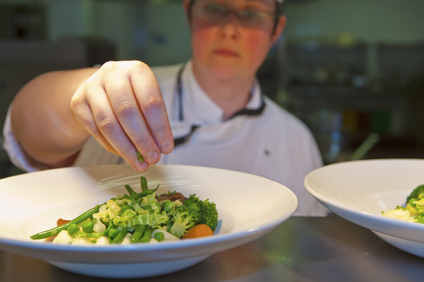 Close-up van chef-kok finishing touch toe te voegen op zijn schotel - Foto, afbeelding