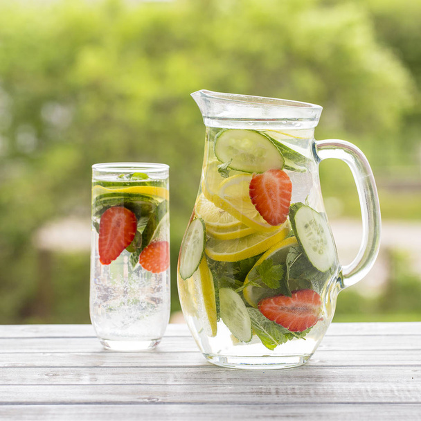 Dietary detox drink with lemon juice, red strawberry, cucumber and mint leaves in clear water with ice. - Photo, Image