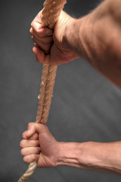 Hands pulling rope over dark background - Photo, image