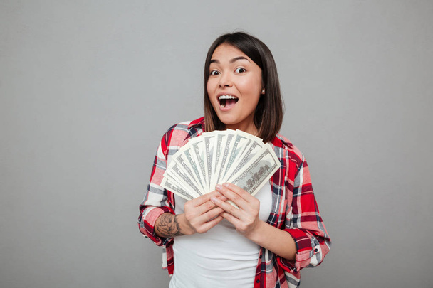 Emotional woman holding money over grey wall. - Zdjęcie, obraz
