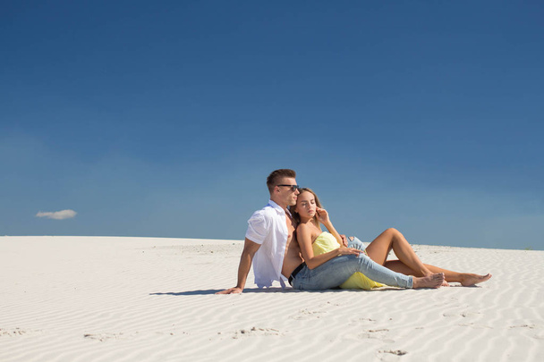 Ξανθό κορίτσι σε ένα ελαφρύ φόρεμα βρίσκεται με έναν φίλο σχετικά με λευκή άμμο - Φωτογραφία, εικόνα