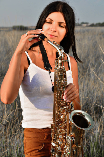 Woman adjusts the saxophone standing in the middle of the field - Photo, image