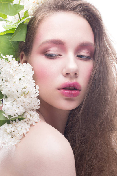 A young girl with lilac and bright creative make-up. Beautiful model with flowers and long hair. White isolated background. Pure shining skin. Beauty of the face - Fotó, kép