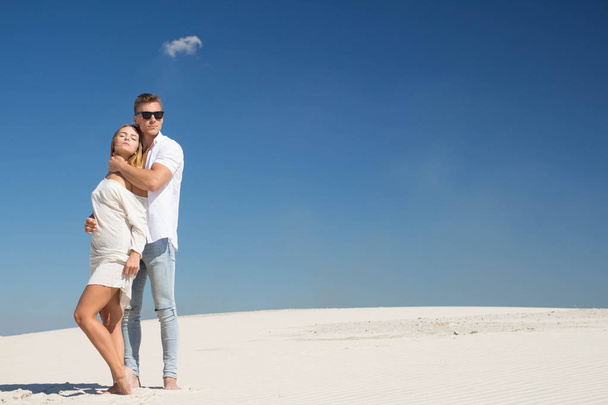 Hyvin kaunis nuori pari seisoo kirkkaan auringon alla valkoisen hiekan keskellä.
 - Valokuva, kuva