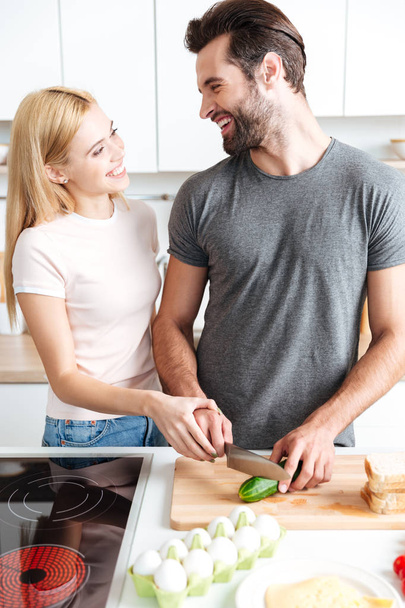 Happy young loving couple standing at kitchen and cooking - Fotografie, Obrázek