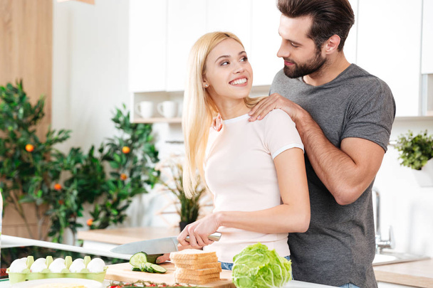 Happy young loving couple standing at kitchen and cooking - Photo, Image