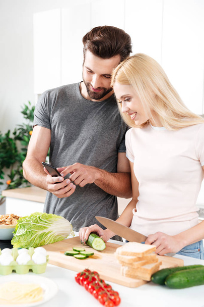 Happy smiling couple using mobile phone to find a recipe - Фото, изображение