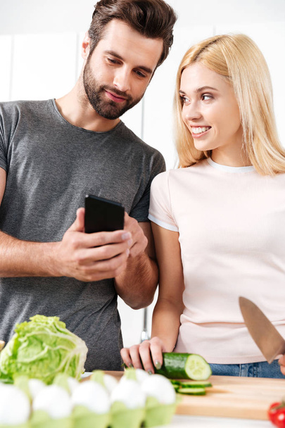 Happy young loving couple cooking together using phone - Foto, Imagem