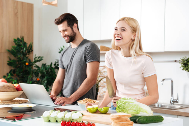 Smiling couple using notebook to cook in their kitchen - Photo, Image