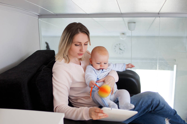 Young mother with baby sits and uses the tablet. Internet browsing, indoor - Foto, Imagen
