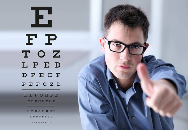 male face with spectacles on eyesight test chart background, showing like hand, eye examination ophthalmology concept - Photo, Image