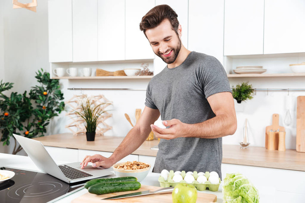 Man with laptop preparing food at the kitchen - Foto, Bild
